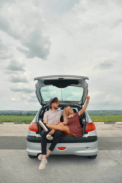 Όμορφο νεαρό ζευγάρι λαμβάνοντας αυτοπορτρέτα στο πορτ-μπαγκάζ αυτοκινήτου — Φωτογραφία Αρχείου