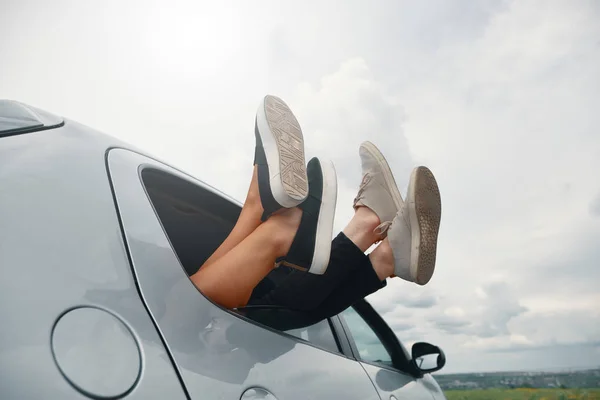 Zwei Beinpaare mit Turnschuhen aus dem Autofenster — Stockfoto