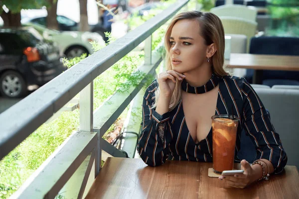 Mulher pensativo sentado em um café com uma bebida fresca segurando um — Fotografia de Stock
