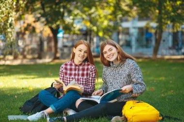 Gülümseyen öğrenciler çimenlerin üzerinde otururken kameraya bakarak poz