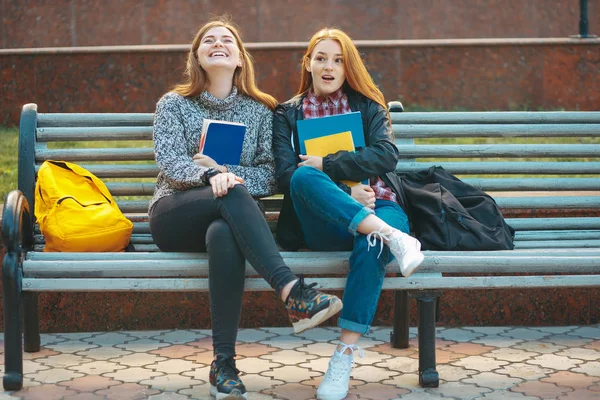 Zwei Mädchen sitzen auf Bank, umarmen Bücher und lachen — Stockfoto