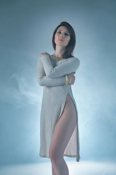 Woman portrait wearing a dress with a deep cut on smoky backgrou