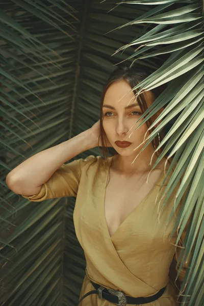 Stunning Woman Posing on Palm Leaves Background. Beautiful Young Exotic Dreamy Female. Portrait. Healthcare. Natural Skin. Face. Big Circular Earrings. Face expression