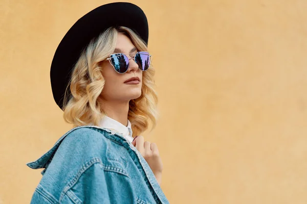 Portrait of Hipster Fashion Girl Holding Jaket on one Shoulder Standing at the Yellow Wall Background. Youth Urban Fashion Concept. Copy Space.