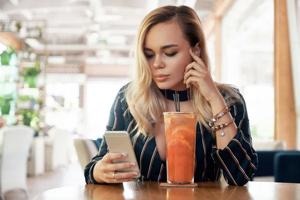 Charming woman with beautiful smile reading good news on mobile phone during rest in coffee shop, happy Caucasian female watching her photo on cell telephone while relaxing in cafe during free time