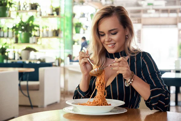 Sensual woman rolling spaghetti and keeping on a fork to eat. Beautiful girl blonde hair and make-up, dine in the restaurant, eating delicious served hot pasta in the cafe. Spaghetti on a fork.