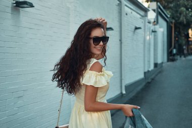 Avrupa'da tatil harcama ilham Bayan portresi. Gülümseyen, neşeli kız sabah şehirde gezdim kahverengi kıvırcık saçlı, güneş gözlüğü, hafif sarı yazlık elbise, açık fotoğraf.