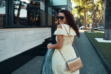 Avrupa'da tatil harcama ilham Bayan portresi. Gülümseyen, neşeli kız sabah şehirde gezdim kahverengi kıvırcık saçlı, güneş gözlüğü, hafif sarı yazlık elbise, açık fotoğraf