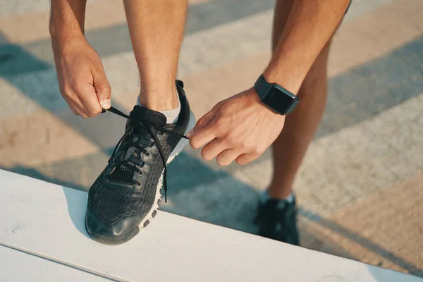 Sportsman ties his black sneakers. Athletic man tying shoelaces while getting ready to run. Smart watch on left hand. Closeup shot