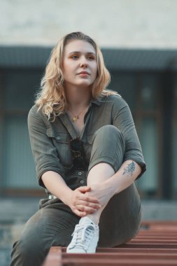 Metal konstrüksiyon ile arka binada oturan bir casual sarışın kız portresi. Genç modern kadın şehirde, açık havada poz. Kentsel yaşam