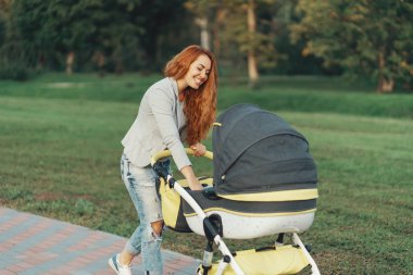 Genç bir anne ile küçük çocuğunu onun bebek arabası rahatlatıcı park yürüyüş zevk.
