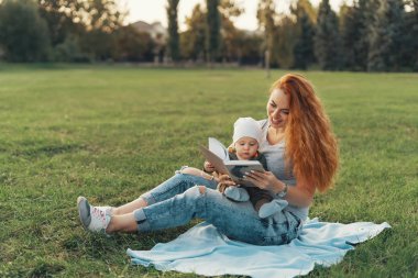 Güzel anne şirin bebek oğlu ile bir kitap okuma ve gülümseyen, çim üzerinde otururken