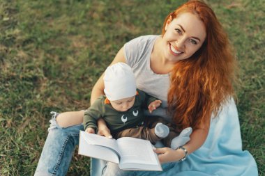Güzel anne şirin bebek oğlu ile bir kitap okuma ve gülümseyen, çim üzerinde otururken