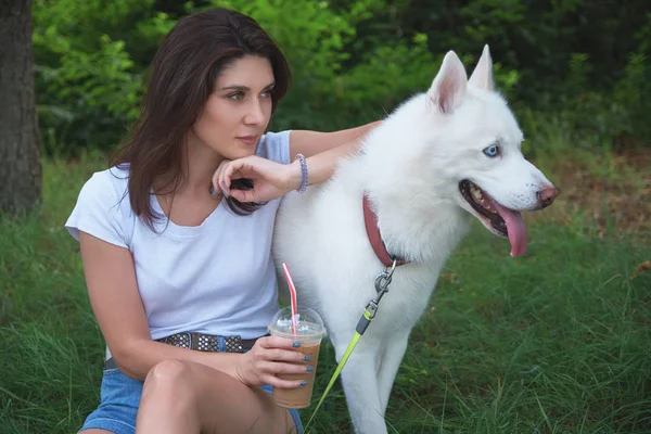 ハスキーな屋外での魅力的な若い女性 女性は彼女の犬と緑の草の上寒い夏の飲み物を飲みながら休憩 — ストック写真