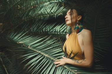 Güzellik kadını. Güzel genç egzotik rüya gibi Her cilt dokunmadan kadın, gözleri kapalı. Portre Palm üzerinde arka plan bırakır. Sağlık. Mükemmel cilt. Yüz. Renkli tüyleri ile büyük dairesel küpeler.
