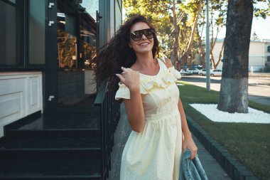 Avrupa'da tatil harcama ilham Bayan portresi. Gülümseyen, neşeli kız sabah şehirde gezdim kahverengi kıvırcık saçlı, güneş gözlüğü, hafif sarı yazlık elbise, açık fotoğraf.