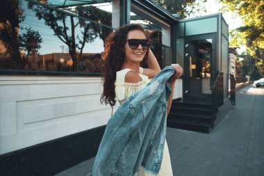 Avrupa'da tatil harcama ilham Bayan portresi. Gülümseyen, neşeli kız sabah şehirde gezdim kahverengi kıvırcık saçlı, güneş gözlüğü, hafif sarı yazlık elbise, açık fotoğraf.