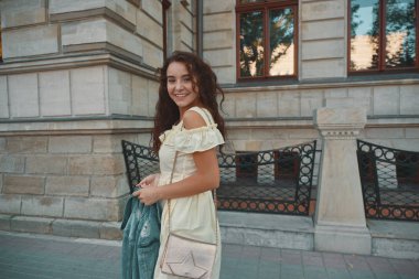 Şık gülümseyen, güneşli, yaz elbise kıvırcık saçlı, çekici, bir sokakta yürüyen mutlu esmer kadın portresi. Genç kadın gülüyor gezgin, neşeli, pozitif,