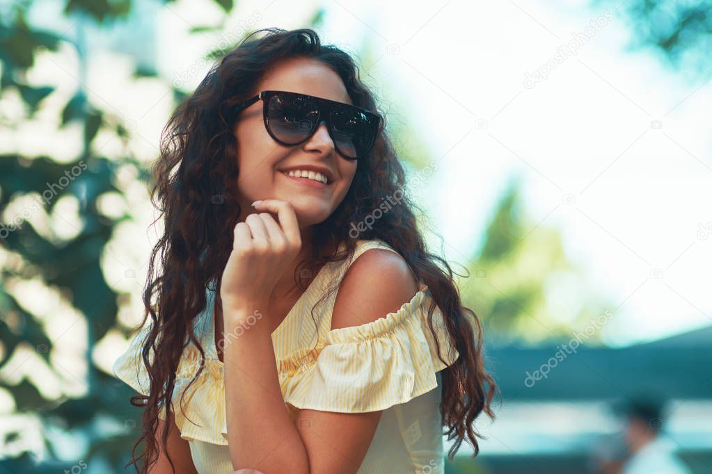 Close-up portrait of beautiful caucasian woman with charming smile walking, posing outdoors.  Model wearing stylish sunglasses. 