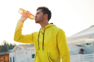 Spor kavram. Adam içme suyu egzersiz kumsalda çalıştırdıktan sonra. Fit vücut çalışan veya eğitim açık sonra dinlenme ferahlatıcı içki içme ile susuz sağlıklı atletik erkek portresi. 