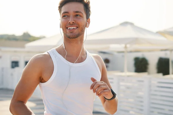 健身运动员跑步者在阳光明媚的日子里奔跑 享受着励志音乐 具有诱人的 完美的微笑的运动男子 积极的生活方式概念 — 图库照片