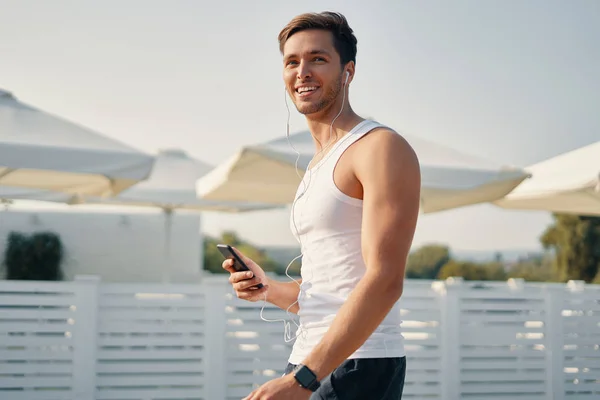 Young handsome runner with smart phone and earphones outside in sunny autumn. Shot of an attractive and sporty young man starting his music play list outdoors.