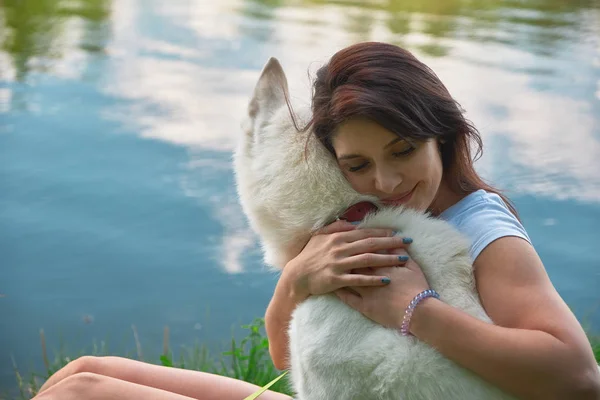 女性は彼女の犬を抱いて 目を閉じ 両手で彼の柔らかい被毛と背景の空を反映して水で顔に触れます 幸福と作品は 友人の最もよい概念 — ストック写真