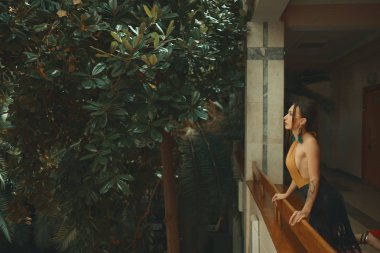 Otel balkonda duran, egzotik ağaçlarıyla çevrili bir tatil zevk dışarı arayan çok şehvetli genç kadın. Dinlenme ve rahatlama kavramı.