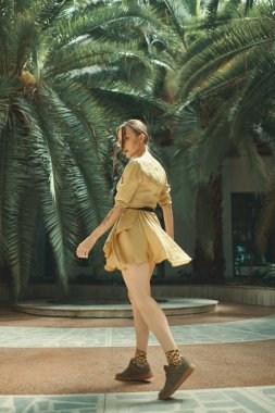 Etkin bir genç dansçı, tropikal bitkiler arka plan üzerinde omuz üzerinden etrafa dönüm büyük palmiye açık havada kalıyor. Orman kıyafeti. Tropikal bahçede yürüyen oynak kadın.