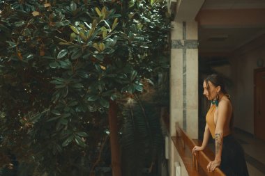 Otel balkonda duran, egzotik ağaçlarıyla çevrili bir tatil zevk dışarı arayan çok şehvetli genç kadın. Dinlenme ve rahatlama kavramı.