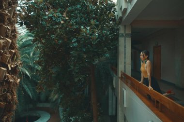 Otel balkonda duran, egzotik ağaçlarıyla çevrili bir tatil zevk dışarı arayan çok şehvetli genç kadın. Dinlenme ve rahatlama kavramı.