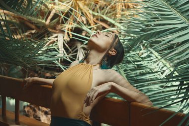 Kadının vücut güzellik ve esneklik. Onun performansı ile kapalı gözler, arka planda tropik bitkiler ile Ahşap korkuluk vücudunda uzanan süre yinelenen kadın dansçı.