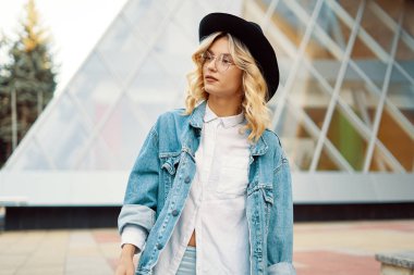 Yakın çekim gözlük camına arka bina şapka ile neşeli beyaz bir kadın portresi. Güzel sarışın saç poz ile moda kız fotoğrafı.