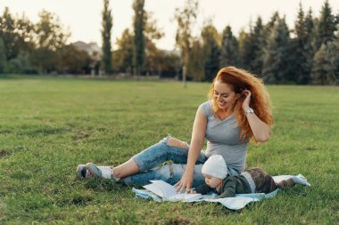 Güzel anne şirin bebek oğlu ile bir kitap okuma ve gülümseyen, çim üzerinde otururken