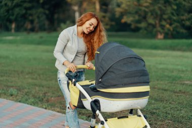 Genç bir anne ile küçük çocuğunu onun bebek arabası rahatlatıcı park yürüyüş zevk.