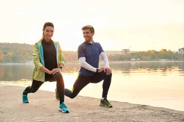 Young running couple warming up and stretching before running outdoors in the morning