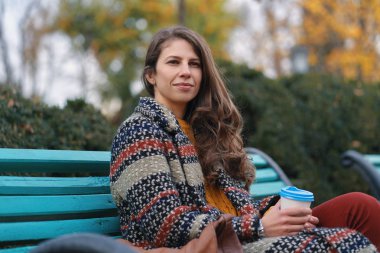 Genç ve güzel kadın güzel havanın tadını iyi ruh hali bir bankta otururken sonbahar gün kahve keyfi.