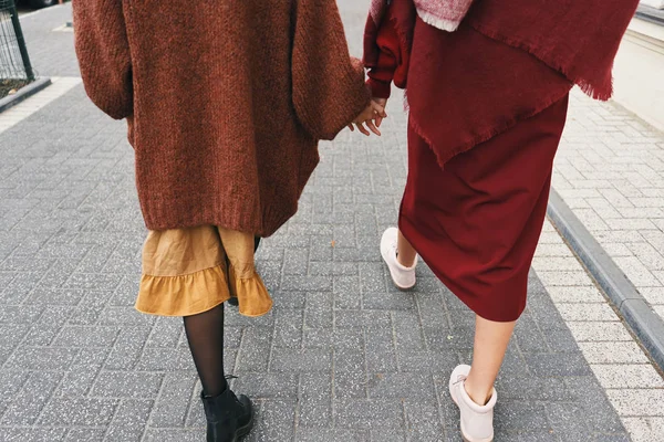 Fall winter fashion outfit details. Back view cropped image of two stylish girls walking on city street. Set of wool clothes, shoes and accessories.