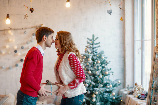 Young couple kissing while holding together a present box, with Christmas decorations in background