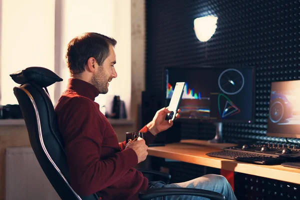 Joven trabajando en el estudio con un smartphone y un ordenador . —  Fotos de Stock