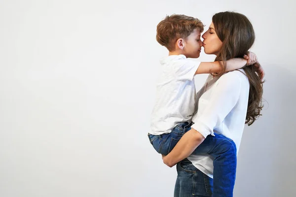 Young mother holding her preteen son smiling and kissing his nose on white background