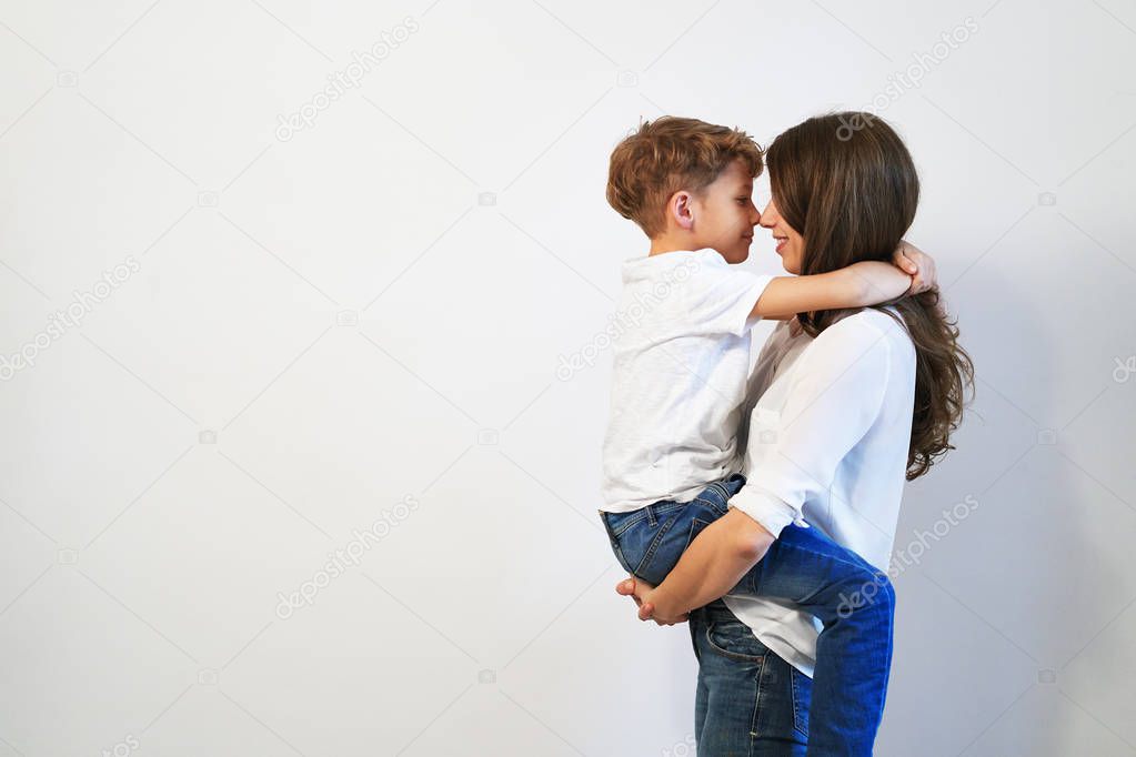 Young mother holding her preteen son smiling and looking into his eyes, touching noses, on white background