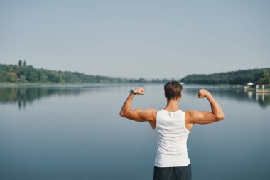 Duygu muzaffer kavramı. Genç adam maratonu kazanan olmak mutlu. Göl arka plan üzerinde güç bir işareti olarak el ele tutuşarak görünümü erkek geri.