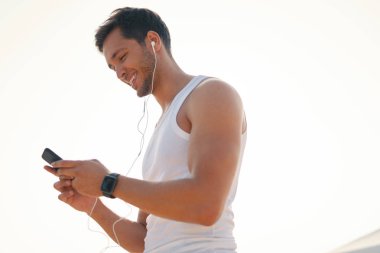 Yakışıklı, mutlu, gülümseyen genç adam akıllı telefon istimal yürüyüş, koşu süre açık havada güneşli, güzel bir günde bir online görüntülü sohbet sahip. Selfie yapma. Yan görünümü. Beyaz arka plan.
