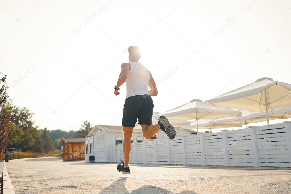 Full length shot of healthy young man running on the promenade in the morning. Male runner sprinting outdoors.