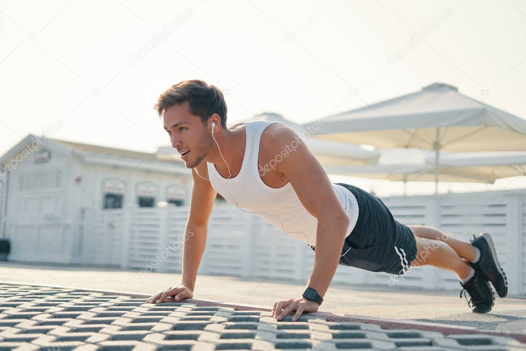Picture of a young athletic man doing push ups, leg over leg listening music outdoors. Strength and motivation. 
