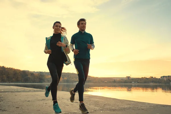 Güneşin doğuşunu göl kenarında bir run için koşucular motive birkaç. Genç erkek ve kadın giyim, birlikte çalışan spor. Sportif insanlar eğitim açık havada