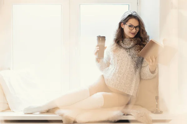 보온병에서 마시고 가벼운 Bokeh와 창틀에 합니다 그녀는 따뜻하고 부드러운 스웨터와 — 스톡 사진