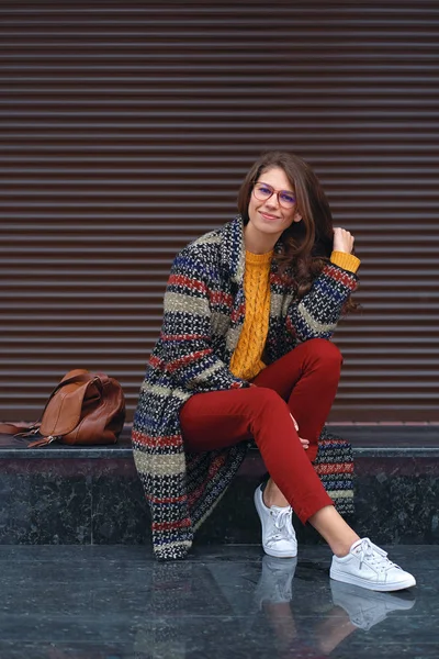 女性の肖像若い 美しいスタイリッシュなコート 赤いパンツをはいて オレンジ色のセーター 茶色の革のバッグと 白いスニーカーを身に着けているヨーロッパの都市の通りでポーズします コピー スペース — ストック写真