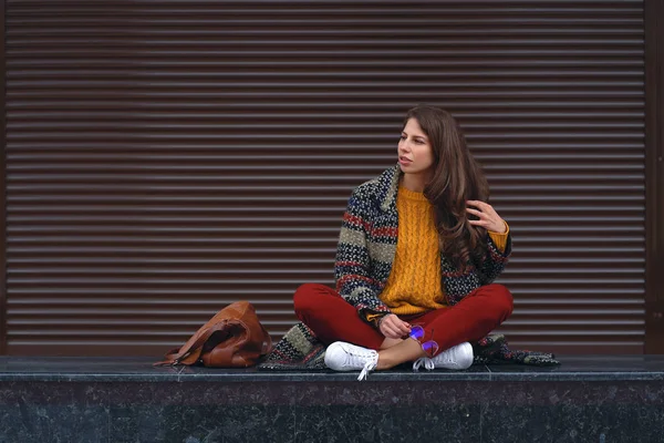 座っている笑顔の若い女性の肖像画胡坐 ヨーロッパの都市の通りでポーズします 右側のバック グラウンドでブラウン コピー スペース — ストック写真